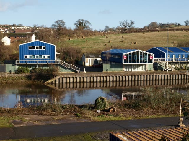Blue boathouses on the bank of the River Dart in winter sunshine, with fields rising behind